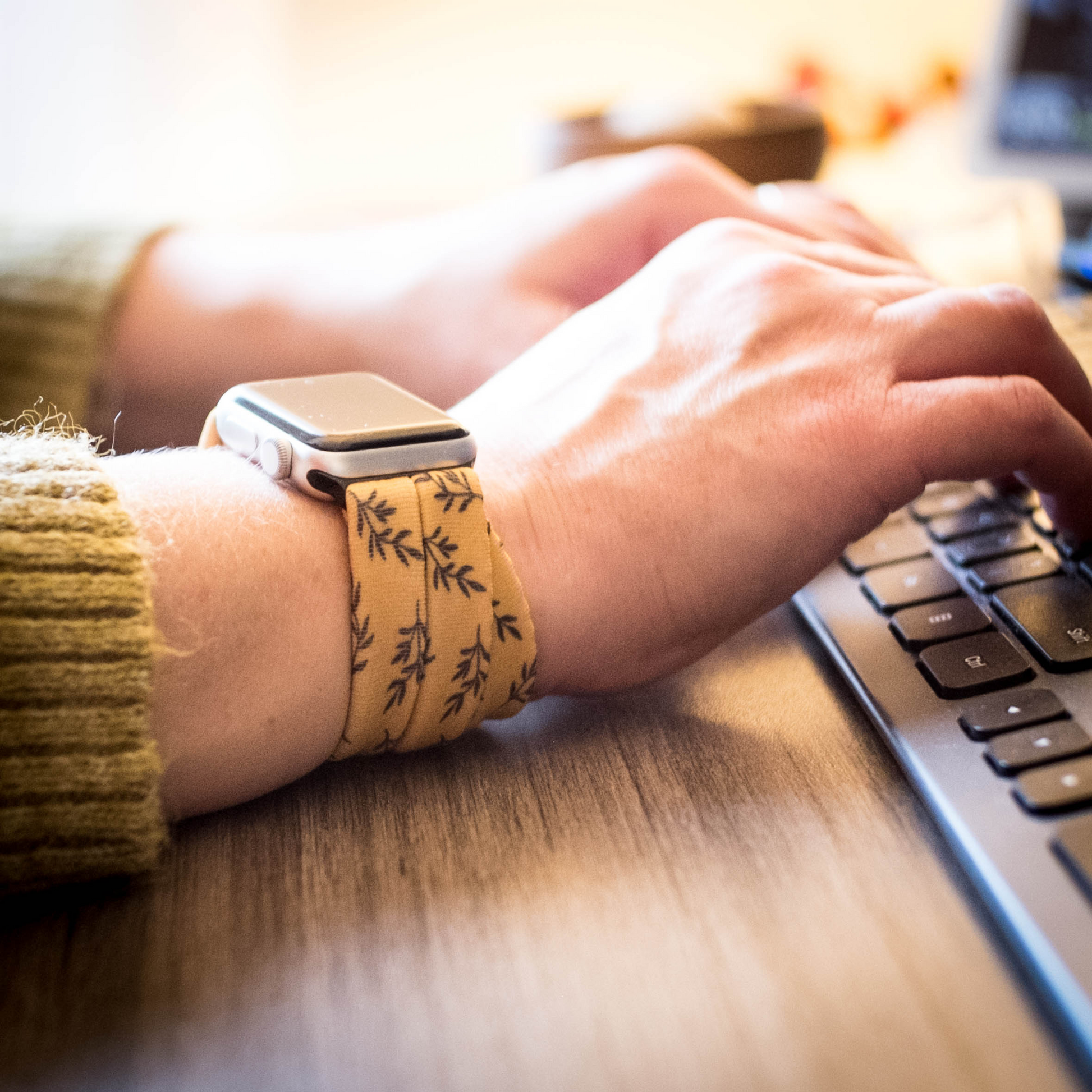 Golden Laurel Yoga Band® featuring a delicate black laurel leaf print on a vibrant goldenrod fabric. A breathable, stretchy watch strap with a patent-pending design compatible with Apple Watch, Fitbit, and Samsung Galaxy models.